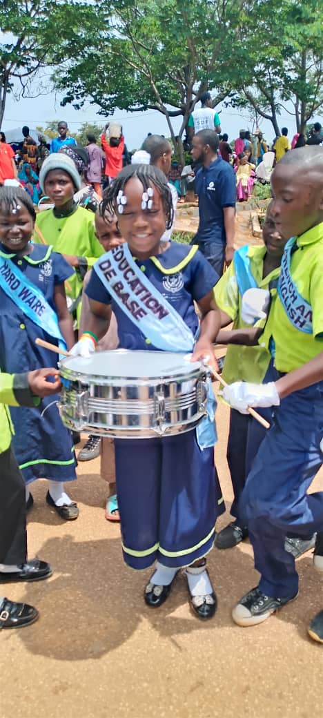 Élève de la fanfare portant une caisse claire, écharpe « Éducation de base », pendant un défilé scolaire.